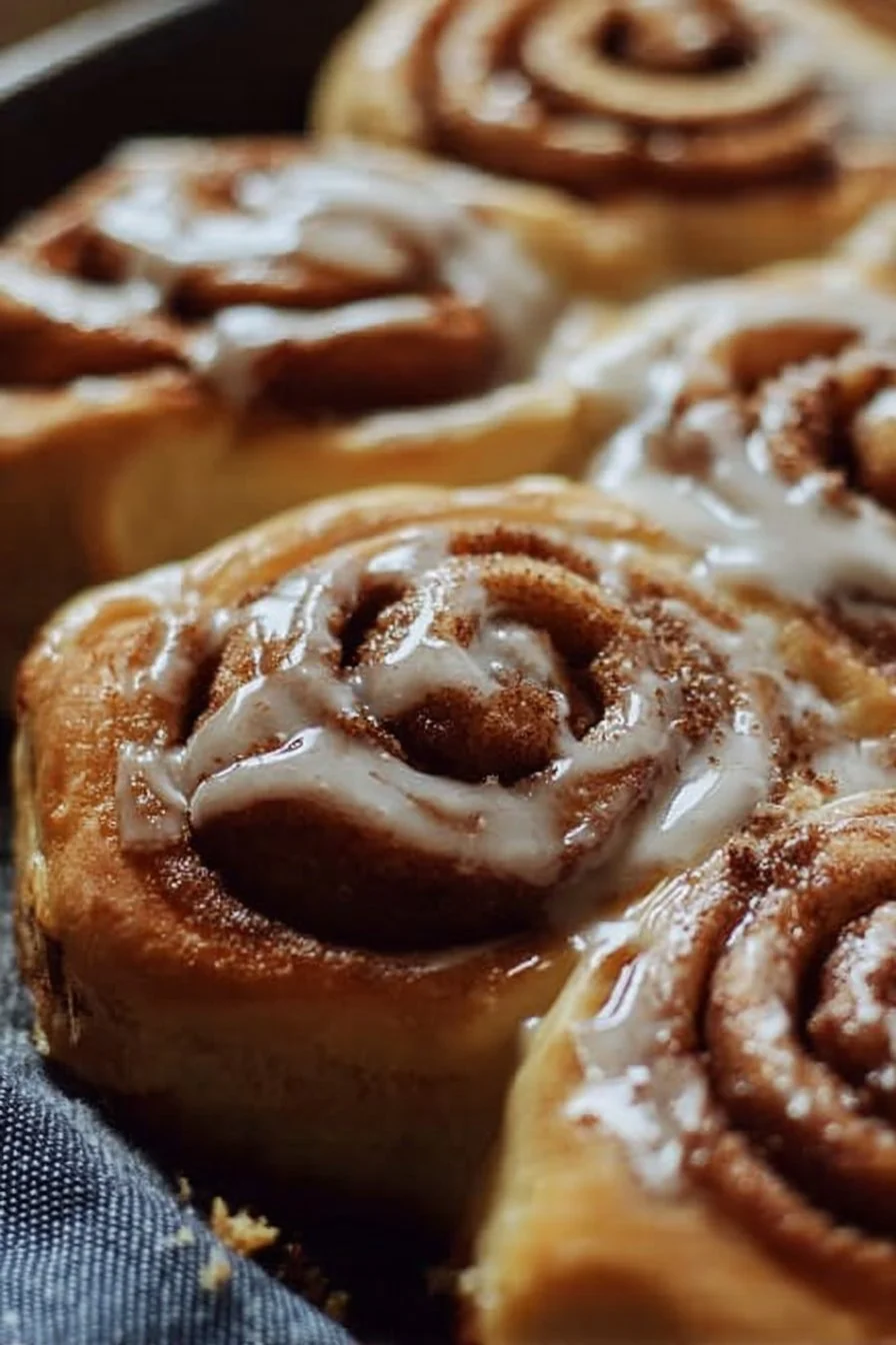 Fluffy sourdough cinnamon rolls topped with icing on a wooden table.