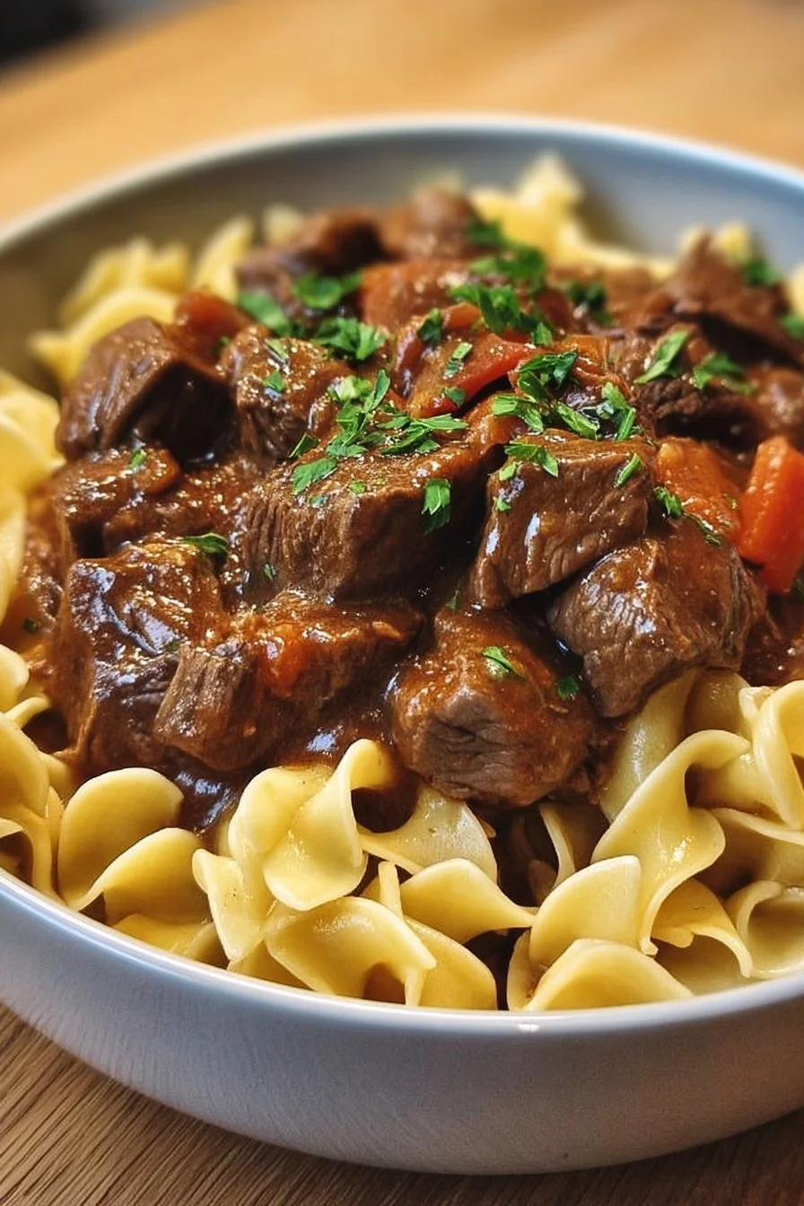 Crockpot beef tips and noodles served in a bowl, garnished with herbs.